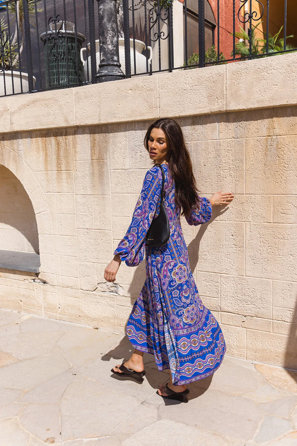 Woman in a blue patterned dress standing against a stone wall.