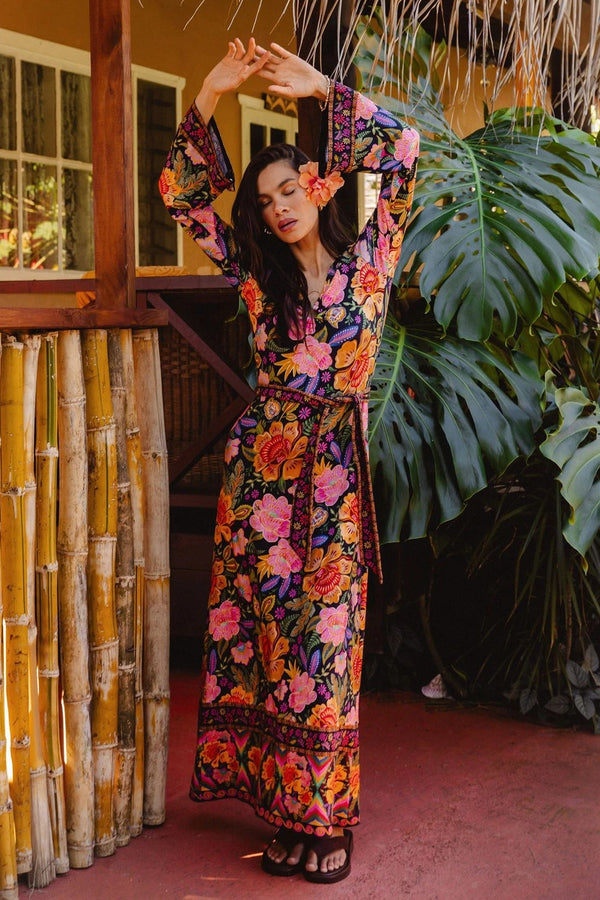 Woman in a colorful floral dress standing on a wooden deck with plants in the background