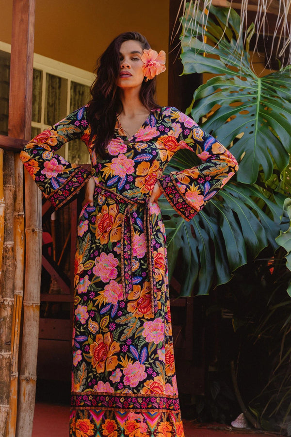Woman wearing a colorful floral dress standing in front of green foliage.