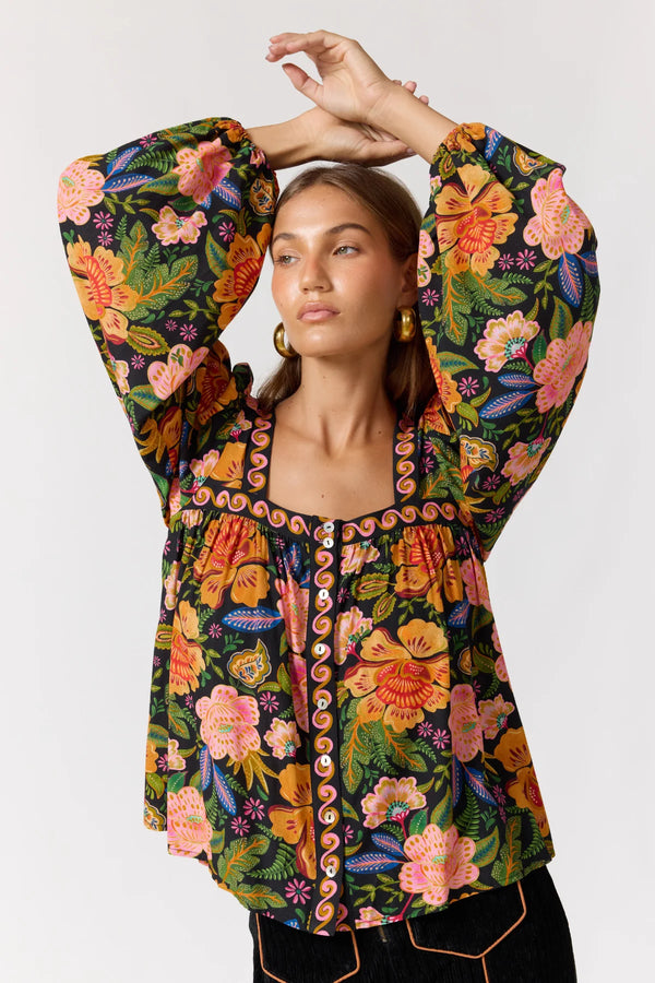 Woman wearing a colorful floral patterned blouse with long sleeves on a white background