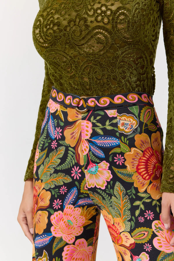 Person wearing a green embroidered top and colorful floral pants on a white background