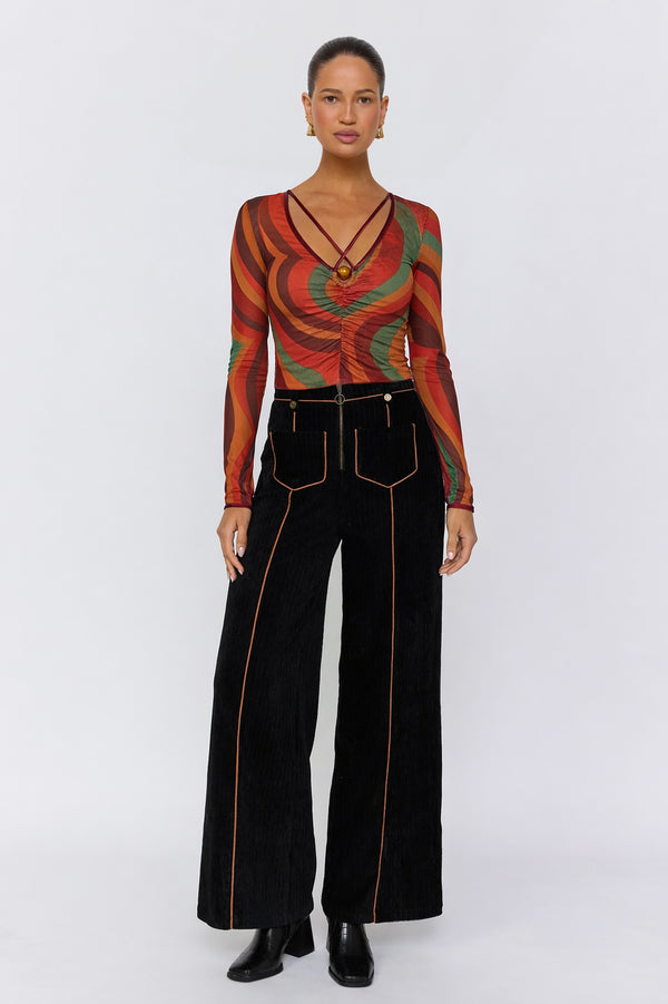 Woman wearing a patterned top and black pants on a white background