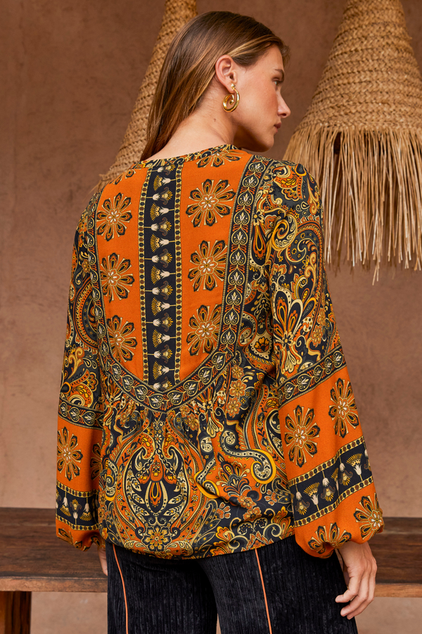 Woman wearing a patterned orange and black blouse against a brown background