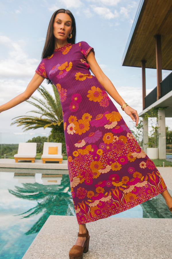 Woman wearing a vibrant floral dress by a poolside with a modern house in the background
