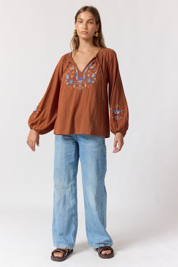 Woman wearing a brown embroidered blouse and blue jeans on a white background