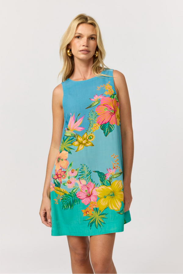 A woman wearing a sleeveless sky blue to aqua shift mini dress with a vibrant tropical hibiscus floral print, shown front on against a light gray studio background.